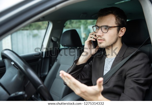 Young guy talking on the phone while sitting at\
his car. Road safety\
concept.