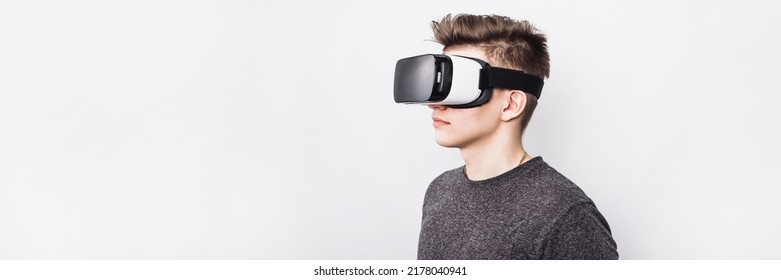 A young guy, a teenager stands in a villard vr glasses on a white background. Augmented reality in our time. A virtual reality glasses boy plays games and learns at school. Web banner.