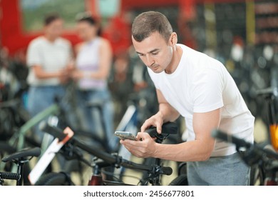 Young guy using smartphone for examining quality seat and choosing bike in modern bicycle sports store - Powered by Shutterstock