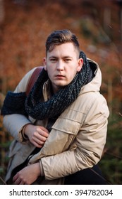 young guy in a warm cap and a jacket with a scarf on the neck, trousers and rubber boots walks alone in the Carpathian mountains with a camera, a tripod and a backpack on his shoulders