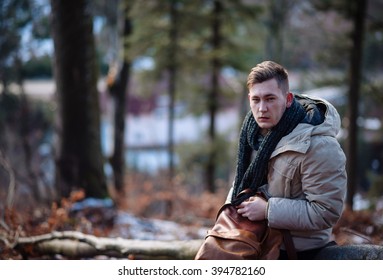 young guy in a warm cap and a jacket with a scarf on the neck, trousers and rubber boots walks alone in the Carpathian mountains with a camera, a tripod and a backpack on his shoulders
