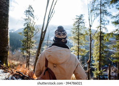 young guy in a warm cap and a jacket with a scarf on the neck, trousers and rubber boots walks alone in the Carpathian mountains 