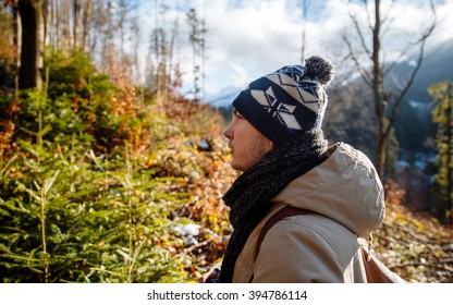 young guy in a warm cap and a jacket with a scarf on the neck, trousers and rubber boots walks alone in the Carpathian mountains with a camera, a tripod and a backpack on his shoulders