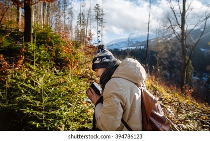 young guy in a warm cap and a jacket with a scarf on the neck, trousers and rubber boots walks alone in the Carpathian mountains with a camera, a tripod and a backpack on his shoulders