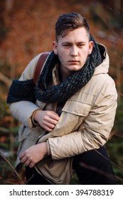 young guy in a warm cap and a jacket with a scarf on the neck, trousers and rubber boots walks alone in the Carpathian mountains with a camera, a tripod and a backpack on his shoulders
