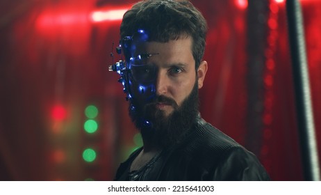 Young guy wearing a headset with LED lights stands behind the black hanging rods and looks at the camera. Cyberpunk and futuristic concept. Neon lights in the background.