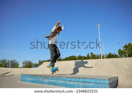 Young guy wearing inline skates doing balancing stunt at skateboard park