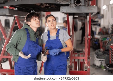 Young guy and young woman mechanics in uniform inspect underbody of car in car service station - Powered by Shutterstock