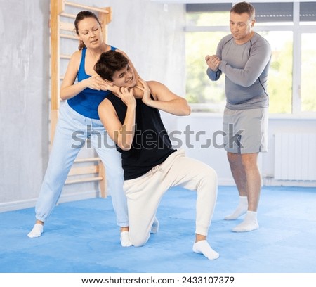 Young guy and woman train to perform effective defense of strangling opponent, while learning self-defense techniques. Lesson in presence of experienced instructor