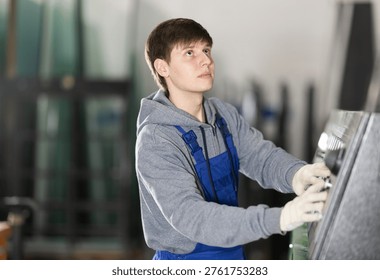 Young guy worker in uniform operates machine control panel in factory