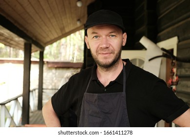 Young Guy Works, Dressed In Black In A Dressing Gown And In A Black Cap. Portrait Of A Young Unshaven Guy In A Black Cap. Guy In A Working Dressing Gown