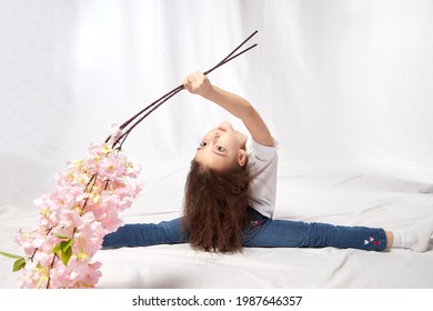 A Young Gymnast Girl With Flowers In The Studio. Teen Athlete Posing And Doing Sports Exercises On A White Background