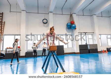 Young gymnast practicing split leap over pommel horse during physical education class, showcasing athleticism and balance in school environment
