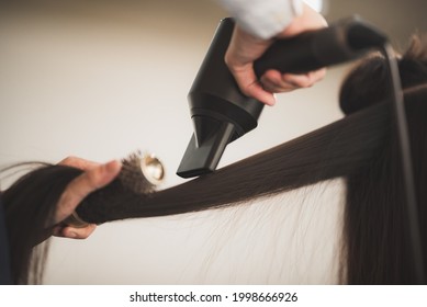 Young hairstylist  drying hair and blowdrying hair of to beautiful long black  hair young woman in beauty salon