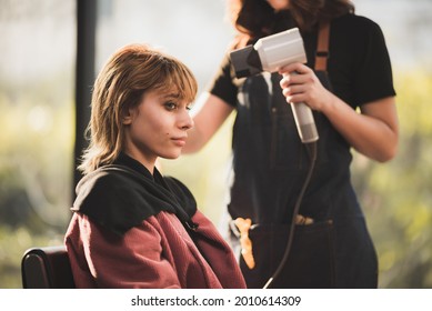 Young hairstylist  drying hair and blowdrying hair of to beautiful short bond hair young woman in beauty salon