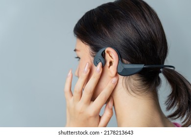 Young half Latina and half Asian woman using bone conduction earphones.