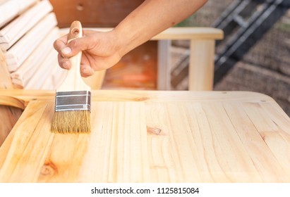 Young Man’s Hand Holding A Brush Applying Varnish Paint On A Wooden Furniture