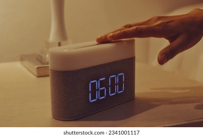 Young woman’s hand turning off digital alarm clock on nightstand in the bedroom at home.