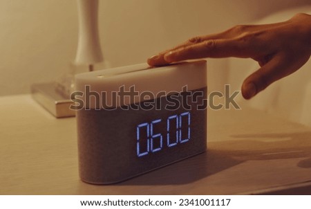 Young woman’s hand turning off digital alarm clock on nightstand in the bedroom at home.