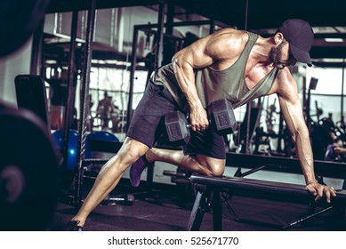 Young handsome adult male doing one-arm dumbbell rows on bench in modern gym - Powered by Shutterstock