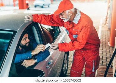 Young Handsome Adult Man Together With Senior Worker Standing On Gas Station And Fueling Car And Paying With Credit Card.