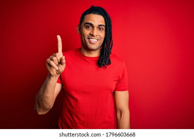 Young handsome african american afro man with dreadlocks wearing red casual t-shirt pointing finger up with successful idea. Exited and happy. Number one.