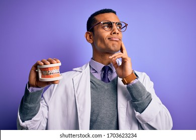 Young handsome african american dentist man holding denture teeth with dental braces serious face thinking about question, very confused idea