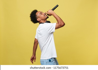 Young Handsome African American Male Singer Performing With Microphone. Isolated Over Yellow Gold Background.