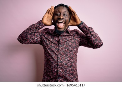Young handsome african american man wearing casual shirt standing over pink background Smiling cheerful playing peek a boo with hands showing face. Surprised and exited