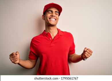 Young handsome african american man wearing casual polo and cap over red background very happy and excited doing winner gesture with arms raised, smiling and screaming for success. Celebration concept