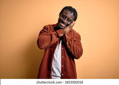 Young handsome african american man wearing casual jacket standing over yellow background sleeping tired dreaming and posing with hands together while smiling with closed eyes. - Shutterstock ID 1853302018