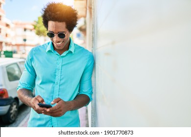 Young handsome african american man wearing casual clothes smiling happy. Leaning on the wall with smile on face using smartphone at town street.