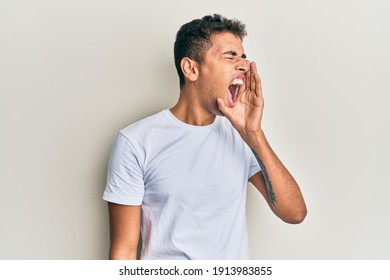 Young handsome african american man wearing casual white tshirt shouting and screaming loud to side with hand on mouth. communication concept. 