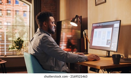 Young Handsome African American Man Working from Home on Desktop Computer in Sunny Stylish Loft Apartment. Creative Male Checking Social Media, Browsing Internet. Urban City View from Big Window.