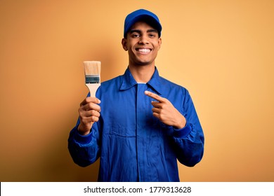 Young handsome african american painter man wearing uniform using painting brush very happy pointing with hand and finger
