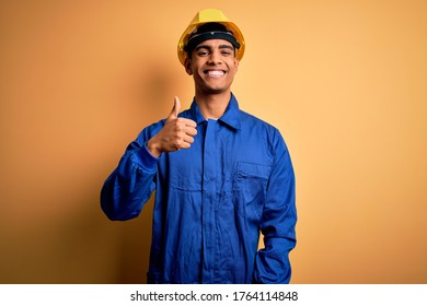 Young handsome african american worker man wearing blue uniform and security helmet doing happy thumbs up gesture with hand. Approving expression looking at the camera showing success. - Powered by Shutterstock