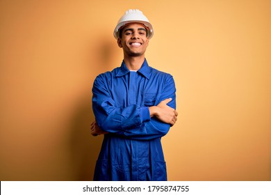 Young Handsome African American Worker Man Wearing Blue Uniform And Security Helmet Happy Face Smiling With Crossed Arms Looking At The Camera. Positive Person.