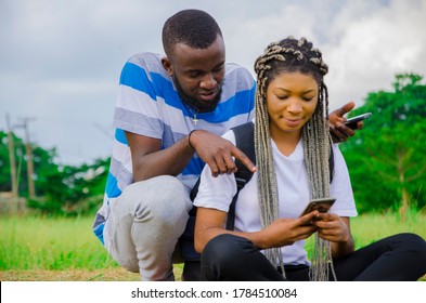 a young handsome african boy squatting behind his girlfriend as she his operating her cellphone, both feeling very excited - Shutterstock ID 1784510084