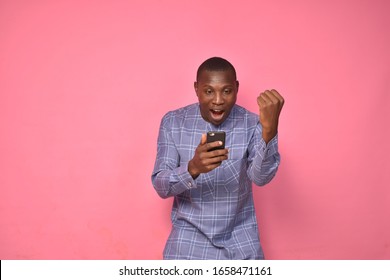 Young Handsome African Man Wearing African Attire Viewing Content On His Mobile Phone, Celebrating