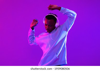 Young handsome African man wearing headphones listening to music and dancing in futuristic purple cyberpunk neon light background