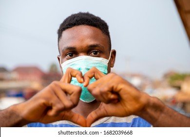 young handsome african nigerian man wore face mask preventing, prevent, prevented himself from the outbreak in his society and did a love sign. - Shutterstock ID 1682039668
