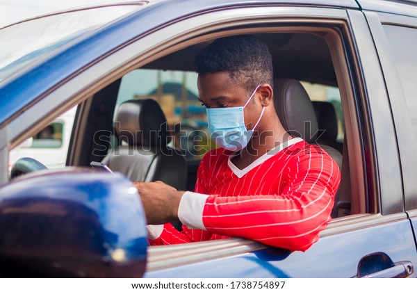 young handsome african taxi driver\
wearing face mask preventing, prevent, prevented himself from the\
outbreak in the society and operating his mobile\
phone