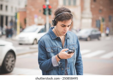 young handsome alternative dark model man in town listening to music with headphones and smartphone connected wireless - Shutterstock ID 250858495
