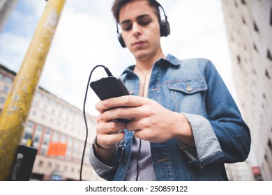 young handsome alternative dark model man in town listening to music with headphones and smartphone connected wireless - Shutterstock ID 250859122