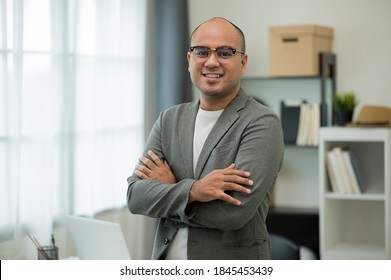 Young handsome asian businessman standing with arm crossed working in office. He was wearing a grey suit and glasses. - Shutterstock ID 1845453439