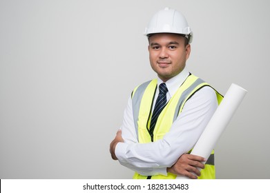 Young handsome asian civil engineer holding paperwork blueprint roll standing post in studio. Worker wearing hard hat on isolated white background.