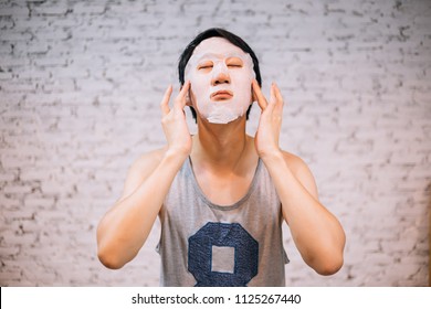 Young handsome Asian man having skincare facial mask on his face at home - cosmetology concept