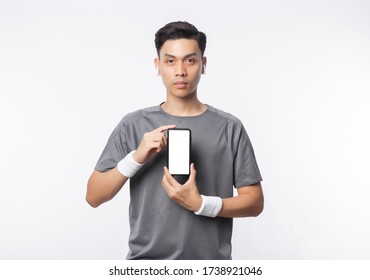 Young Handsome Asian Man In Sport Outfits Showing Phone With Blank Screen And Listening Music Isolated On White Background.