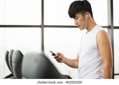 Young Handsome Asian Man Using Smartphone In Modern Gym