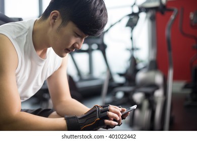 Young Handsome Asian Man Using Smart Phone In Modern Gym